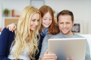 Happy young family using a laptop computer together to browse the internet or social media as they relax together on a sofa at home, parents and a pretty little girl